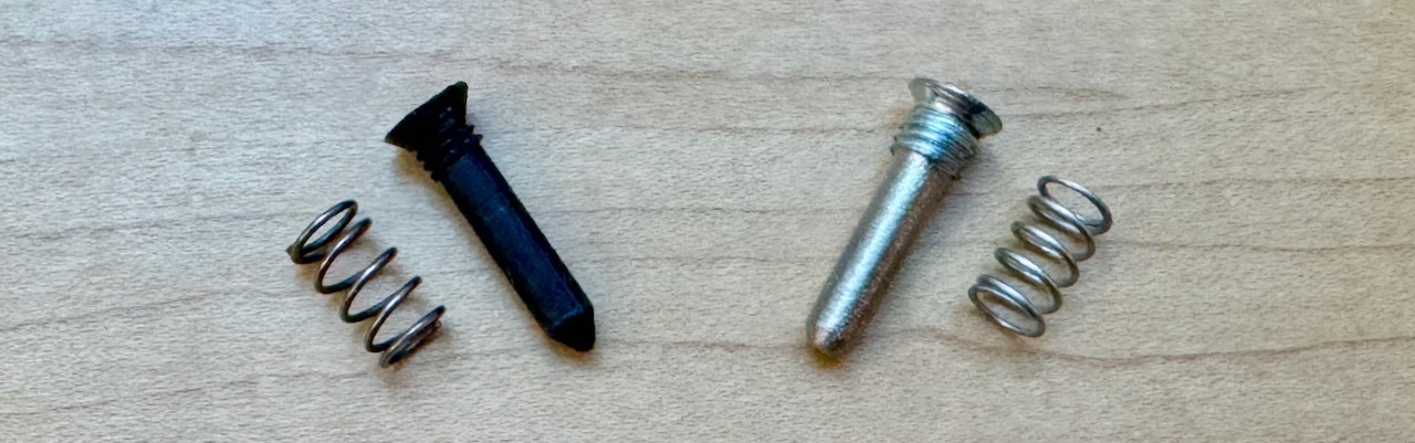 An original plastic pin and spring next to its metal replacement